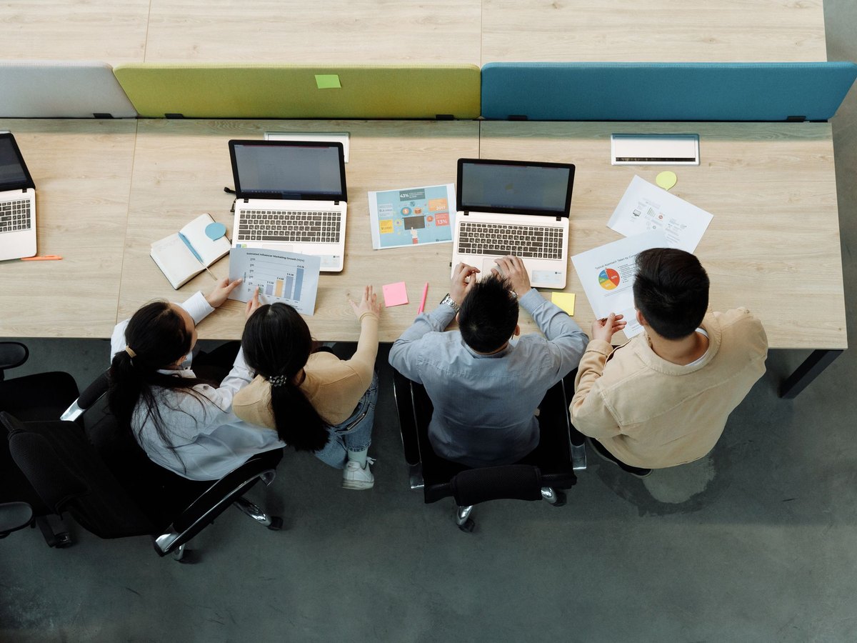 Small team working together at a table with laptops and printed charts